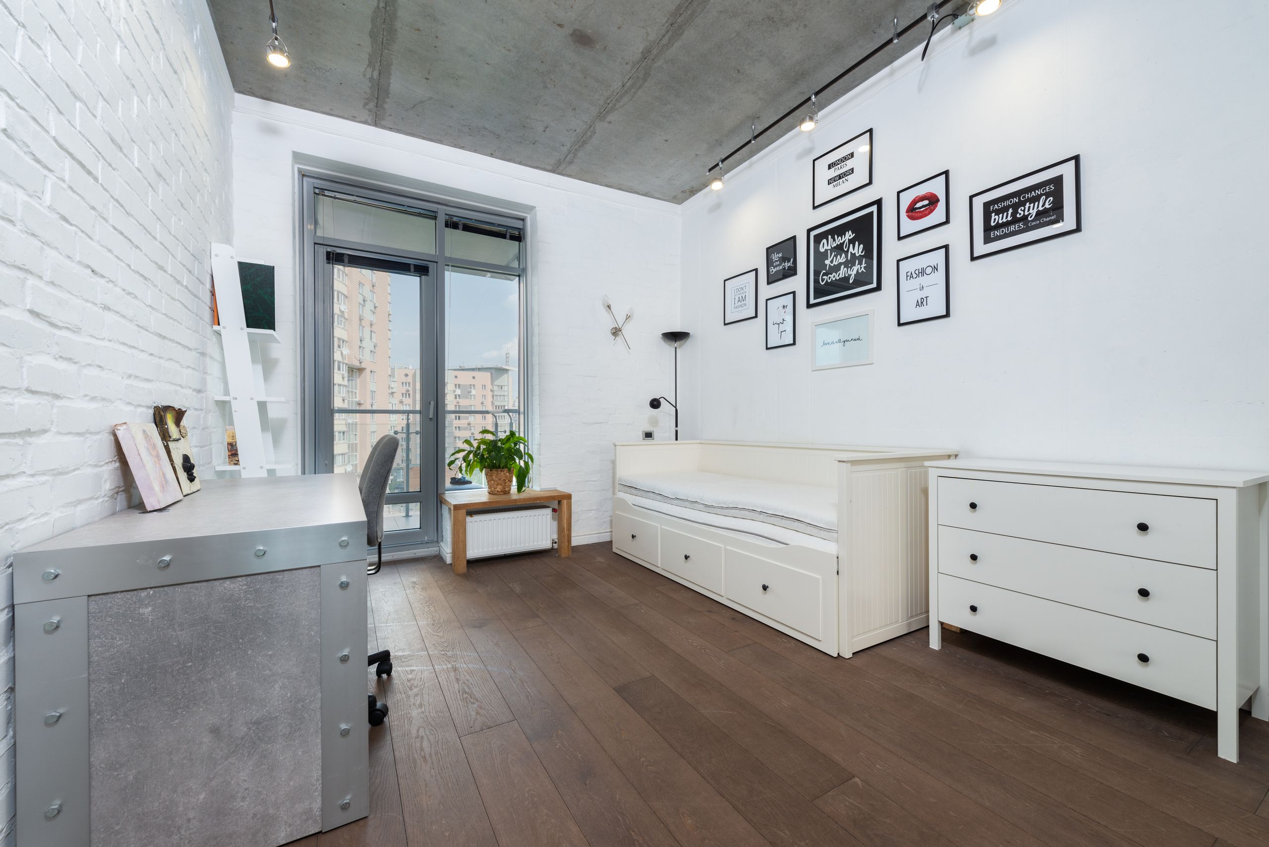 Stylish home office with modern decor, daylight, and art pieces on a white brick wall.